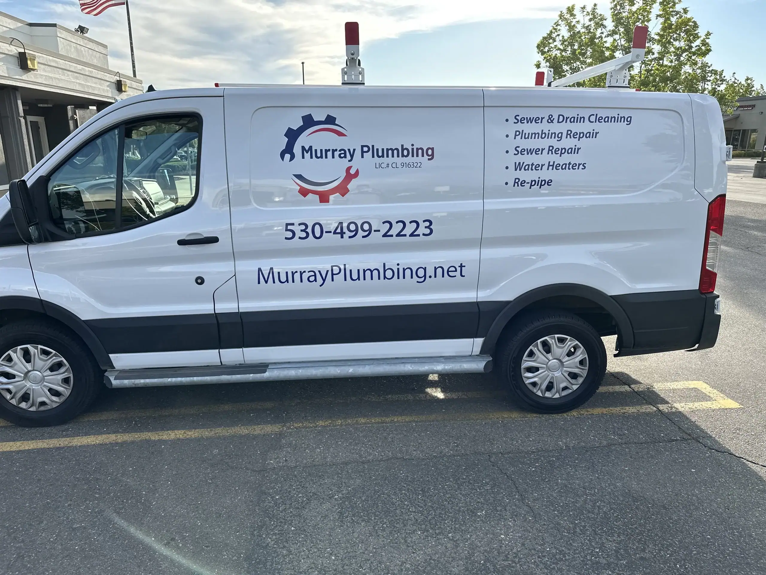 A white Murray Plumbing van is parked in a lot. The company logo, contact number, website, and a list of services, including sewer and drain cleaning, plumbing repair, and water heaters, are displayed on the side.