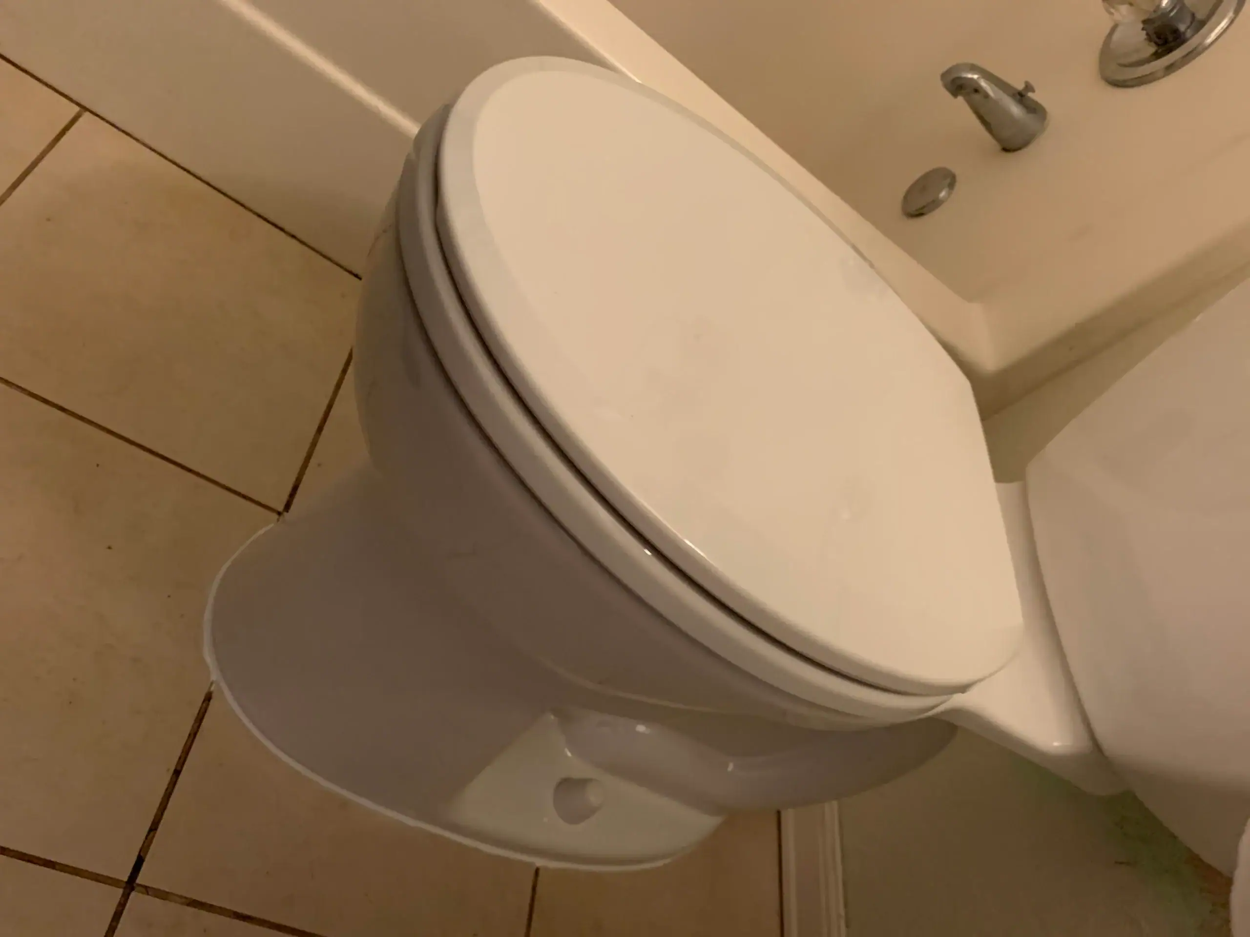 A white toilet with the lid closed sits beside a tiled floor and a beige wall, perfect for any home or bathroom upgrade by a plumber in El Dorado County, CA.