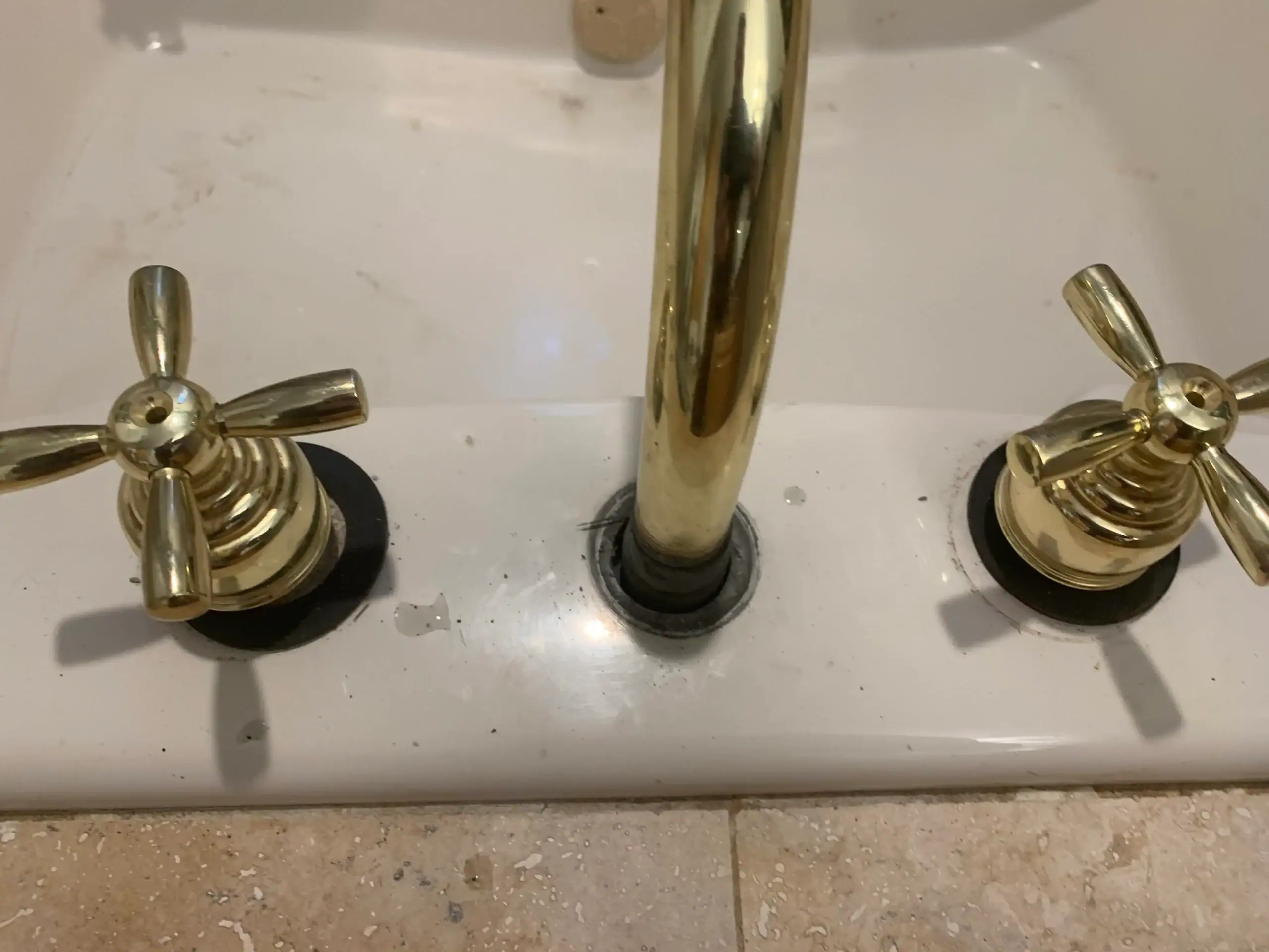 Close-up of a bathroom sink with gold-colored faucet and cross-handle knobs, set on a white countertop. The surface shows water spots and some wear—details often checked by an experienced plumber El Dorado County, CA residents trust.