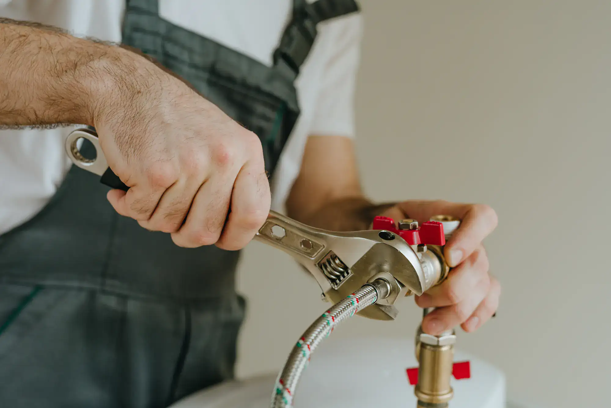 A plumber El Dorado County wearing overalls uses a wrench to tighten a fitting on a metal pipe connected to a water heater or plumbing system.
