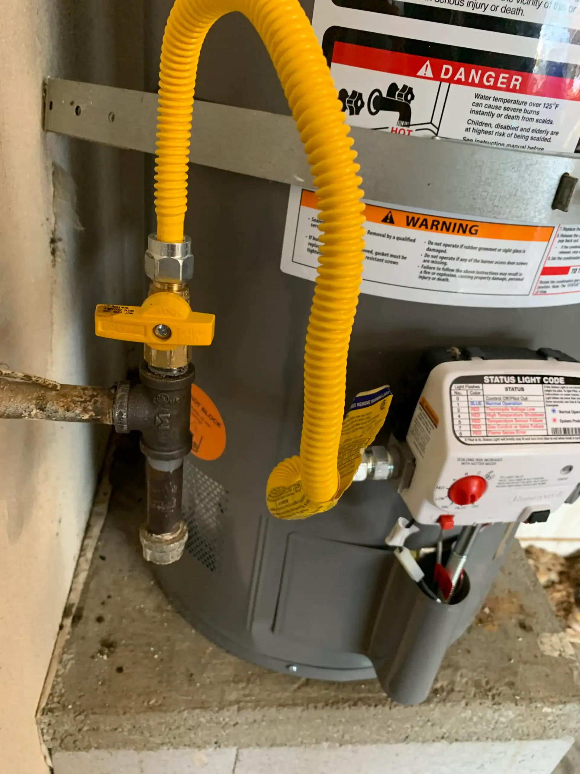 Close-up of a water heater with a yellow flexible gas line, shut-off valve, warning labels, and status control panel. Installed on concrete blocks. For water heater replacement El Dorado County, trust a local plumber El Dorado County, CA.