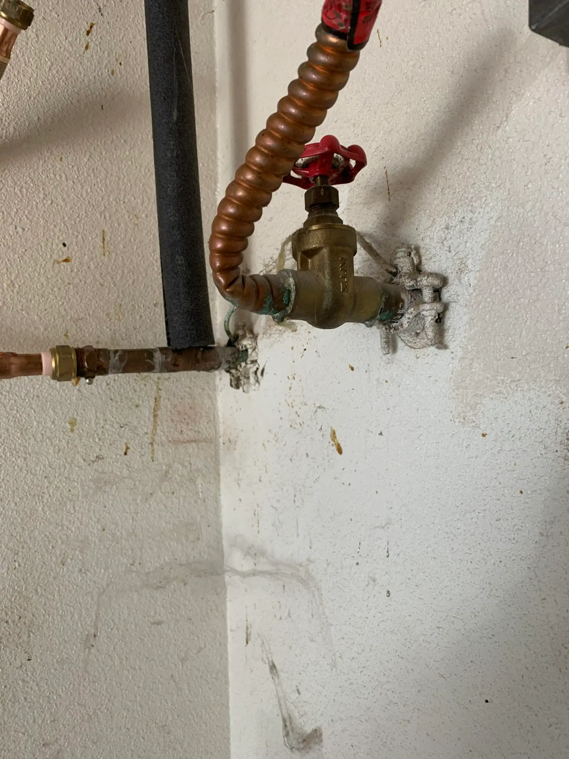 A brass water shut-off valve with a red handle is mounted on a white wall. Copper pipes connect to the valve, showing corrosion and white residue—common signs that may require a plumber El Dorado County for inspection or water heater replacement El Dorado County, CA.
