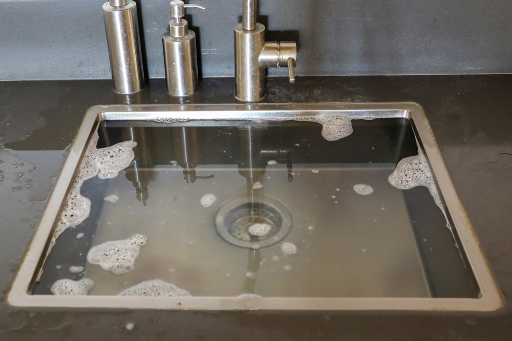 A stainless steel kitchen sink filled with soapy water and bubbles, along with soap and lotion dispensers and a faucet on a dark countertop—an inviting scene where a plumber El Dorado County, CA could lend their expertise.
