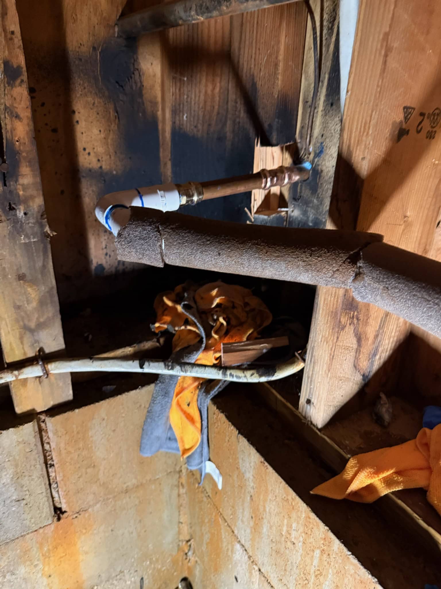 A close-up of exposed pipes and insulation in a wooden wall with burn marks and scorch stains, along with a few rags hanging on the pipes—possible signs that call for a plumber El Dorado County, CA, to inspect or handle water heater replacement.