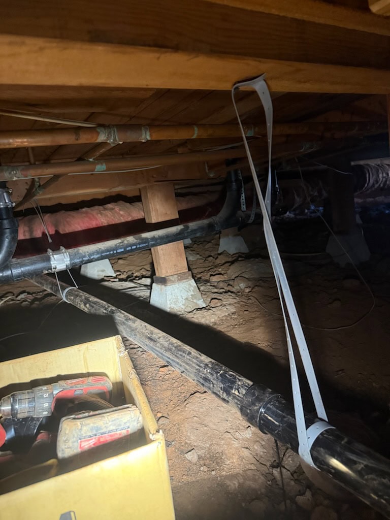 A crawl space beneath a building in El Dorado County shows exposed pipes, wooden beams, and support columns. A plumber’s yellow toolbox is partially visible—ideal for water heater replacement or repairs in El Dorado County, CA.