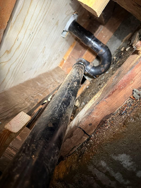 A close-up view of black plumbing pipes running through a wooden structure, with surrounding wood beams and exposed earth or concrete—typical work handled by a skilled plumber in El Dorado County, CA.