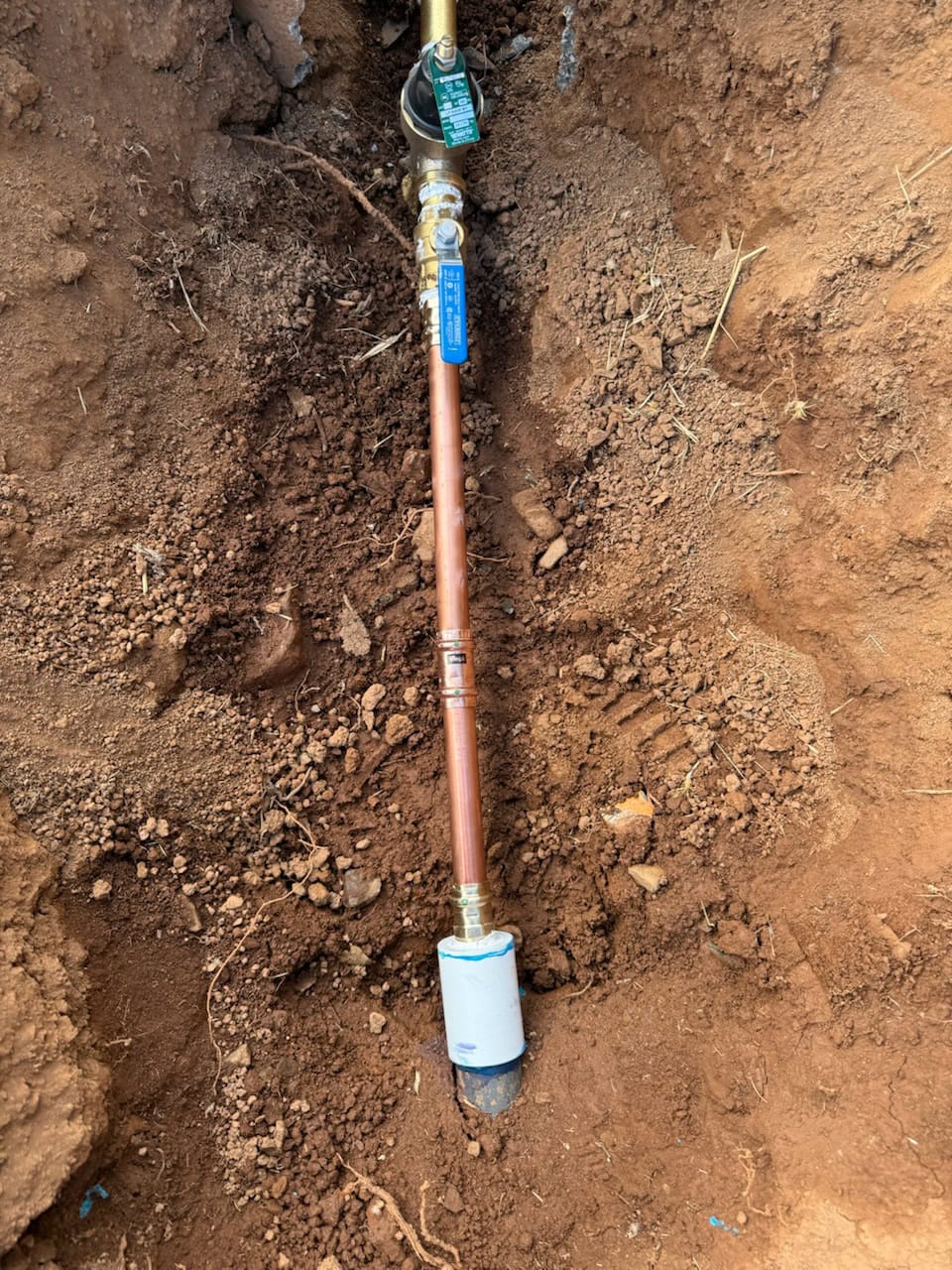 A copper water pipe with a blue-handled shut-off valve is partially buried in soil, with loose dirt around it, suggesting recent installation or repair by a plumber El Dorado County, CA.