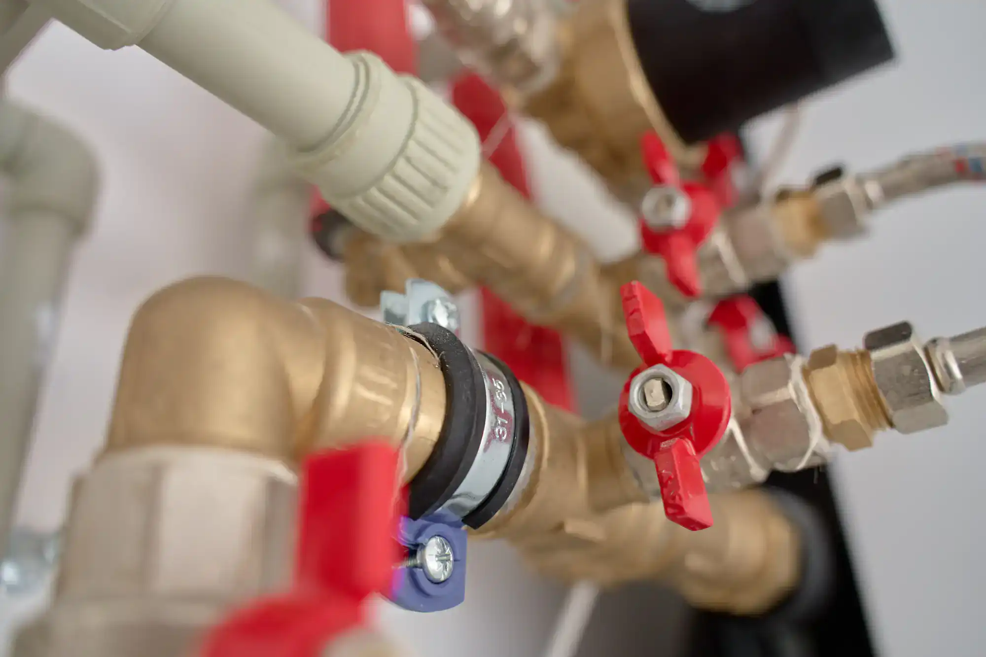 Close-up view of brass plumbing pipes and valves, including several red-handled shut-off valves and metal connectors, forming part of a water or heating system.