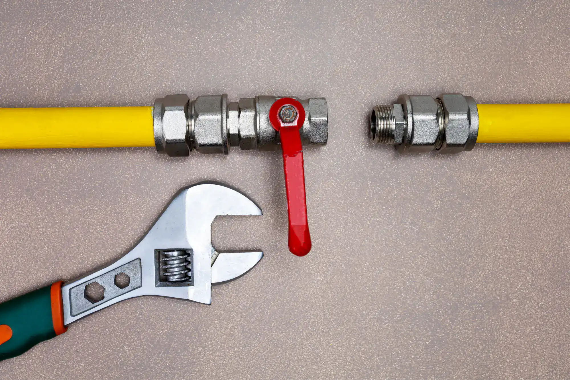 An adjustable wrench and an unconnected gas pipe with a red valve handle lie on a flat surface, showing the process of assembling or repairing the pipeline.