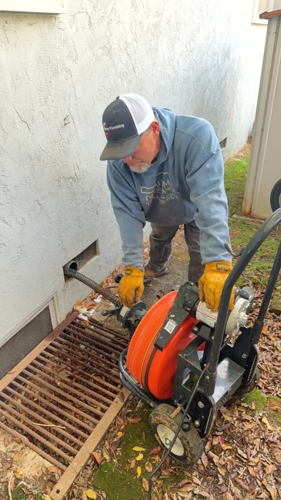 A technician working with drain-clearing equipment at the toilet connection.
