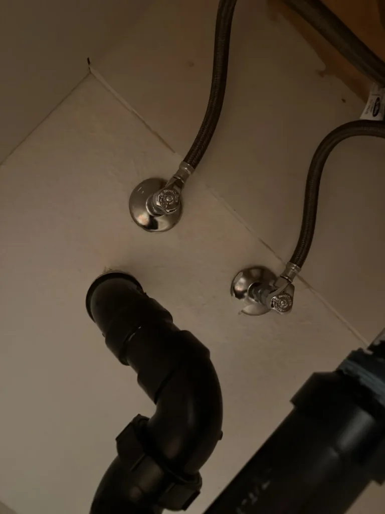 The bathroom faucet supply lines and shutoffs beneath the sink.